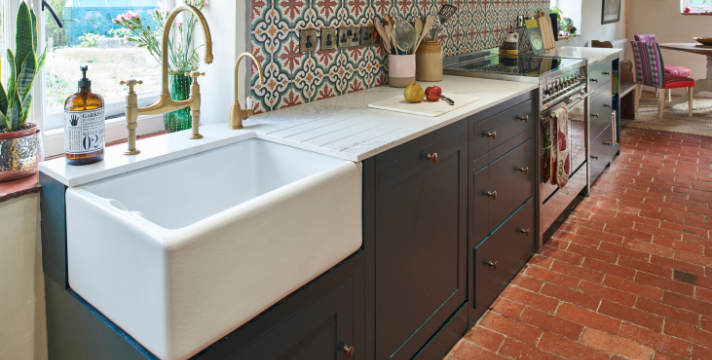 Rustikale Landhausküche mit freistehender Keramikspüle, gemusterten Fliesen und moderner Ausstattung Große weiße Keramikspüle in einer Landhausküche mit bunten Fliesen, dunklen Unterschränken und Blick auf den Essbereich