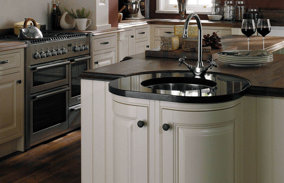 Moderne Einbauküche mit Insel, dunkler Arbeitsplatte und Edelstahlherd Helle Einbauküche mit Kochinsel, rundem Spülbecken, Holzarbeitsplatten, Edelstahlherd und Esstisch mit Weingläsern