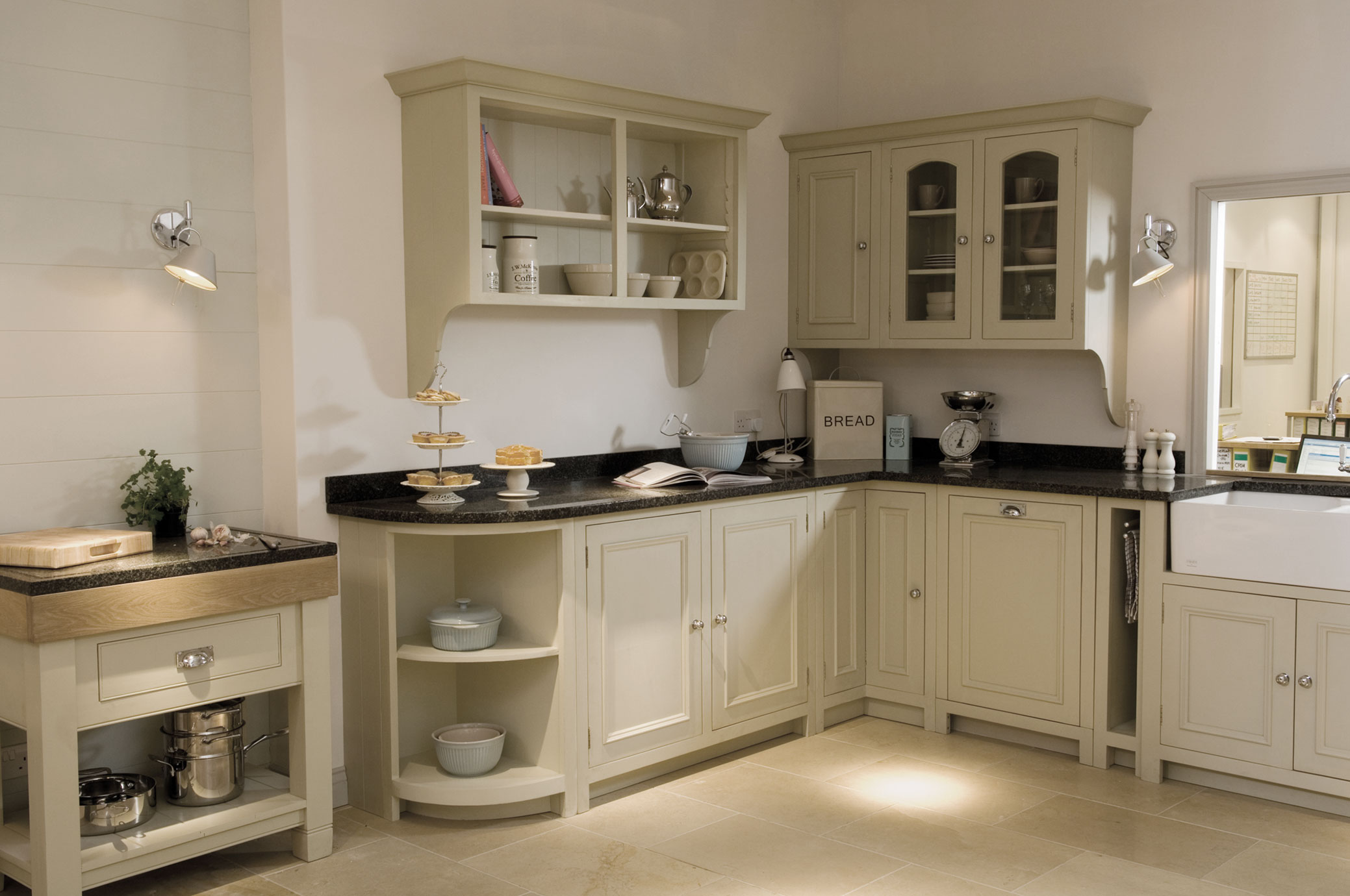 Landhausstil Küche mit cremefarbenen Fronten, schwarzen Arbeitsplatten und modernen Einbaugeräten Gemütliche Landhausküche mit cremefarbenen Schränken, schwarzen Arbeitsflächen, Wandregalen und Küchengeräten, dekorativ eingerichtet