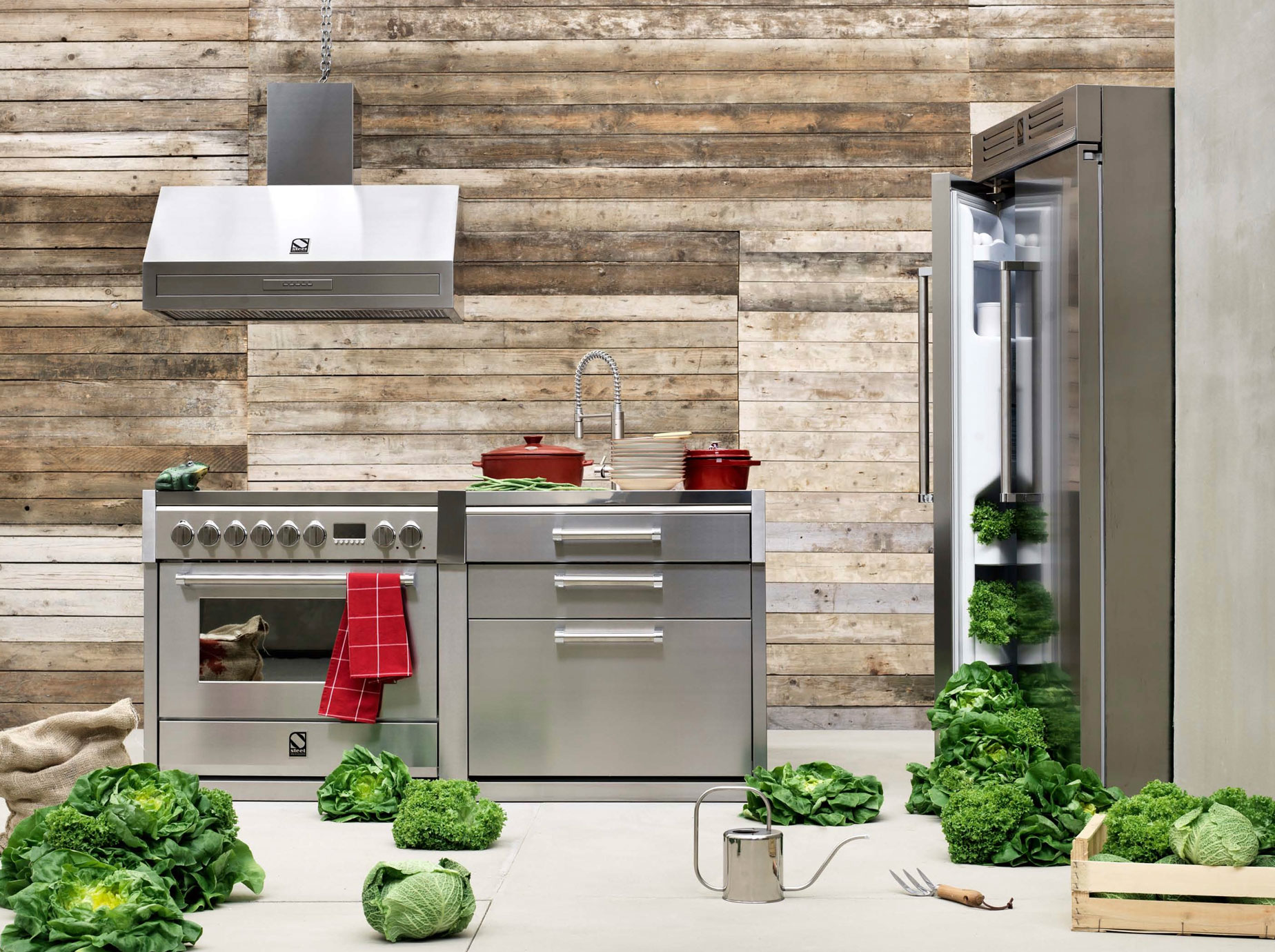 Moderne Edelstahlküche mit offenem Kühlschrank, frischem Gemüse und rustikaler Holzverkleidung Küche aus Edelstahl mit Herd, Spüle und offenem Kühlschrank, dekoriert mit viel frischem grünen Gemüse und Holzwand im Hintergrund