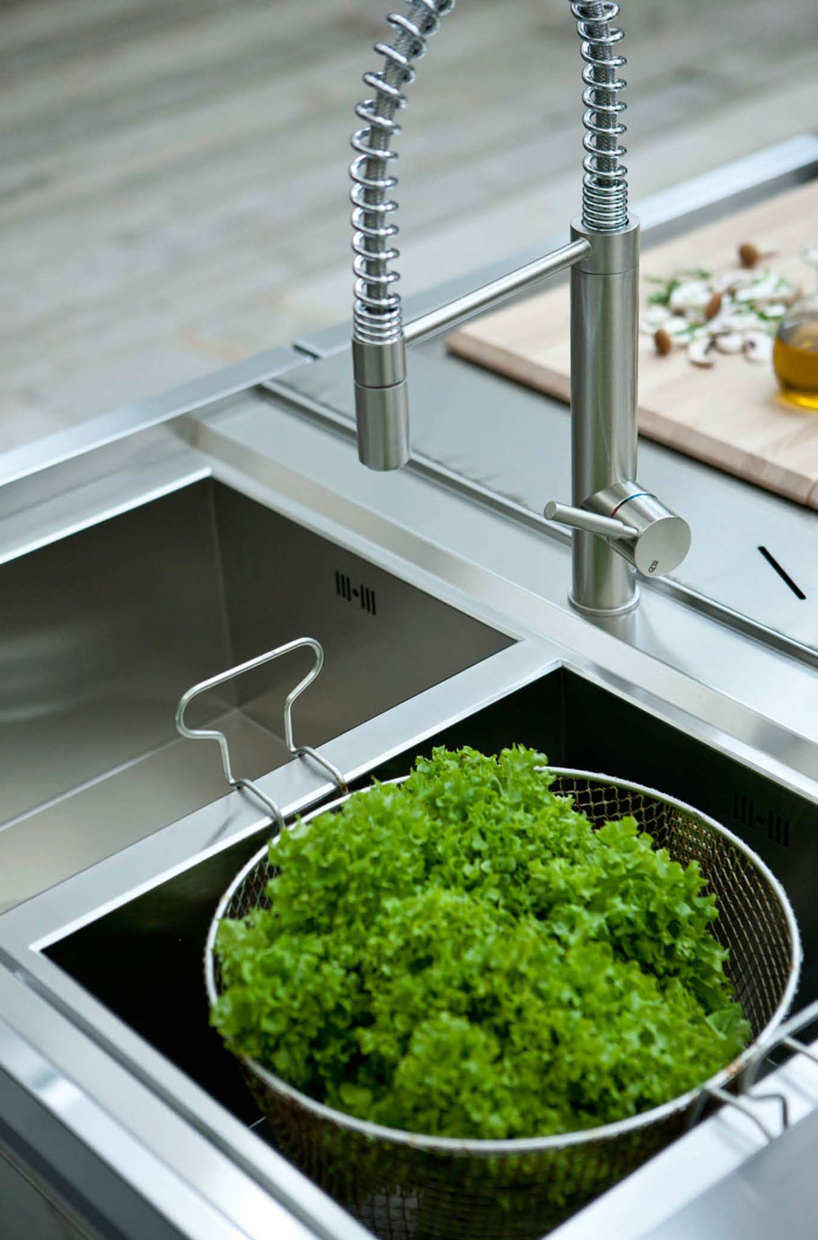 Moderne Edelstahl Spüle mit flexiblem Wasserhahn und frischem Salat in Sieb Edelstahl-Küchenspüle mit flexiblem Wasserhahn und grünem Salat im Abtropfsieb