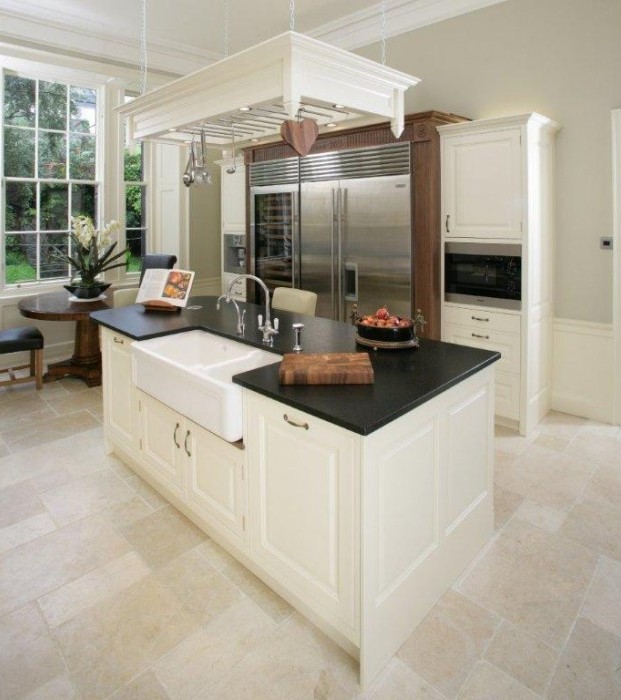 Moderne Landhausküche mit Kücheninsel, Spülbecken und großer Edelstahl-Kühl-Gefrierkombination Helle, moderne Küche im Landhausstil mit Kücheninsel, schwarzer Arbeitsplatte, großem Spülbecken, Edelstahl-Kühlschrank und stilvoller Einrichtung