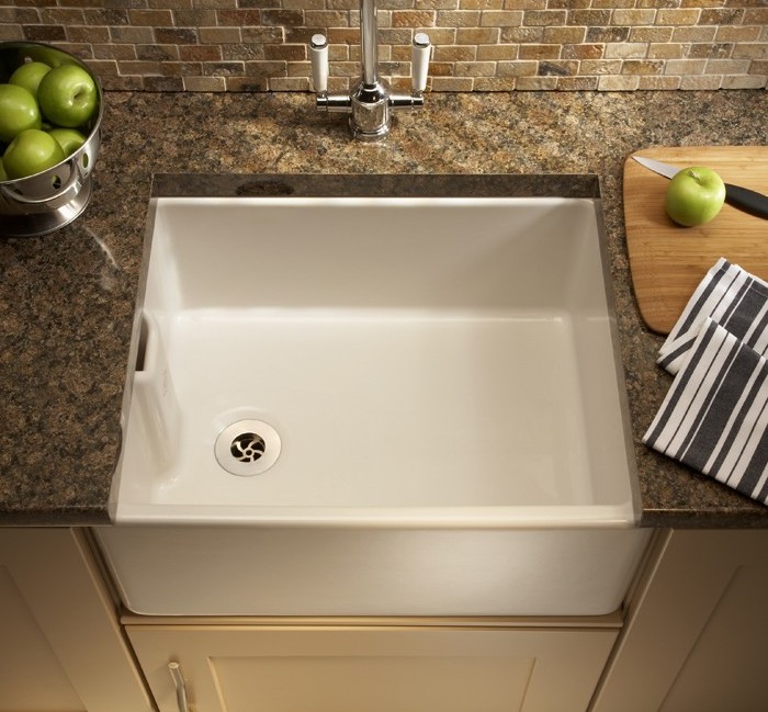 Moderne weiße Küchenspüle mit Granit-Arbeitsplatte und Edelstahlarmatur Weiße Spüle in einer Küche mit granitfarbener Arbeitsplatte, daneben eine Schale mit grünen Äpfeln, ein Schneidebrett mit Apfel und Messer sowie ein gestreiftes Küchentuch