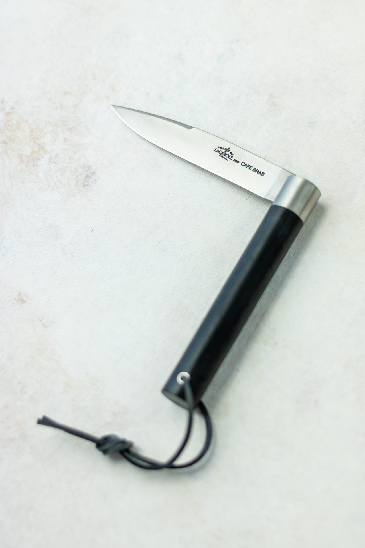 Elegantes französisches Taschenmesser mit schwarzem Griff und Lederband Aufgeklapptes französisches Taschenmesser mit schwarzem Griff und Lederband auf hellem Untergrund