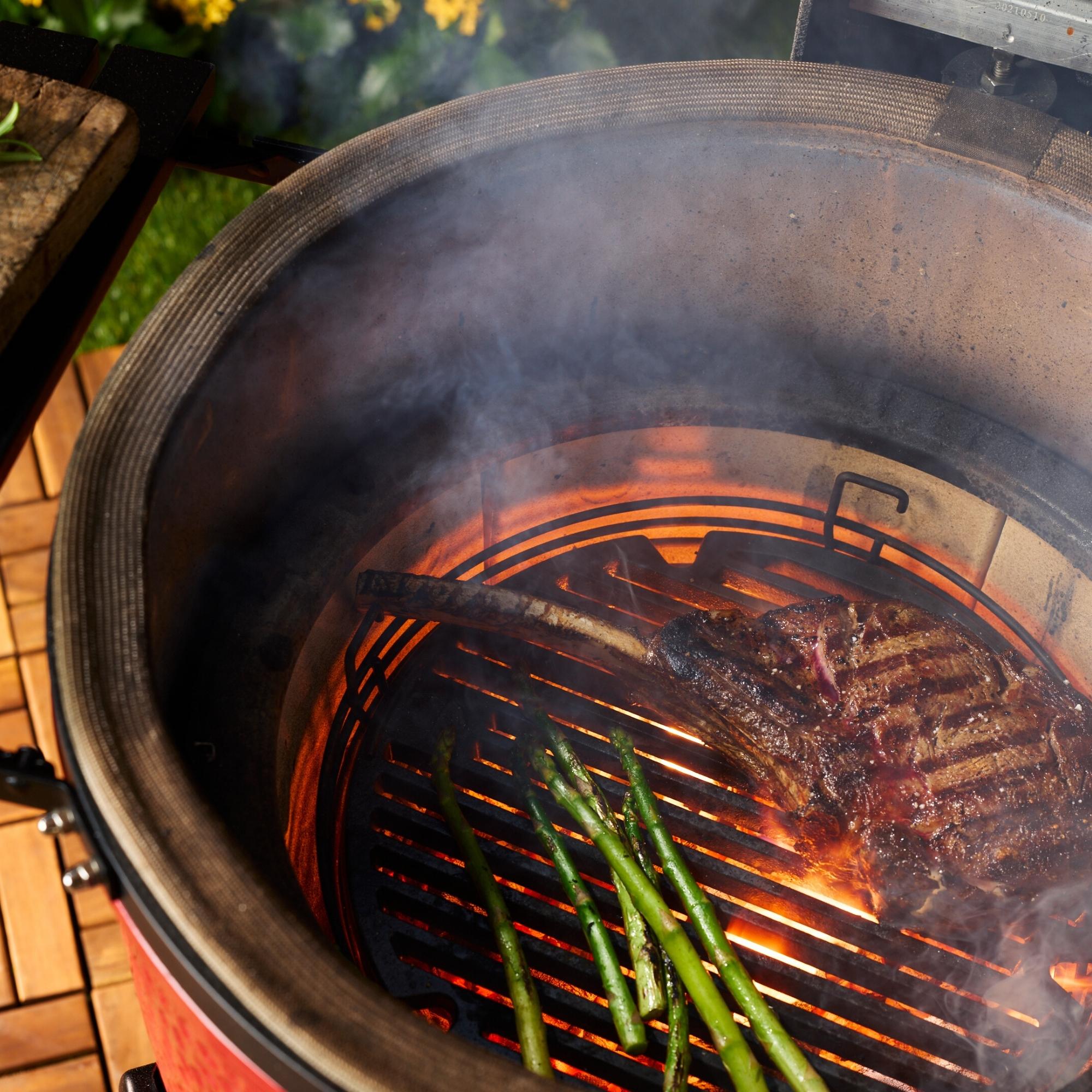 Saftiges Tomahawk-Steak und grüner Spargel auf einem Grill mit heißer Glut und Rauch Ein Tomahawk-Steak und mehrere grüne Spargelstangen werden auf einem Grill bei starker Hitze und offener Flamme gegrillt