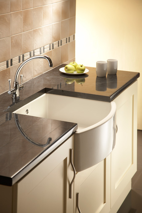 Moderne Küche mit schwarzer Arbeitsplatte, Keramik-Spülbecken und dekorativer Aufstellung Küchenspüle mit abgerundetem Keramikbecken, glänzender schwarzer Arbeitsplatte, zwei Tassen und einem Teller mit grünen Äpfeln auf der Arbeitsfläche