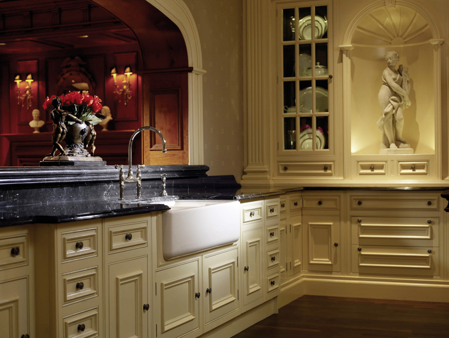 Luxuriöse klassische Küche mit cremefarbenen Schränken und schwarzer Marmorarbeitsplatte Elegante Küche im klassischen Stil mit cremefarbenen Holzmöbeln, schwarzer Marmorarbeitsplatte, nostalgischem Spülbecken und eingebauter Statue