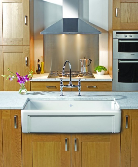 Moderne Küche mit Spüle im Landhausstil, Holzschränken und Edelstahlgeräten Küchenzeile mit weißer Landhaus-Spüle, Holzfronten, Edelstahl-Herd und -Backofen sowie Dekoration mit Blumen und Kräutern