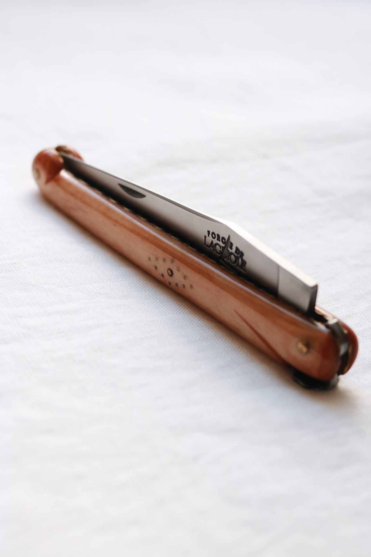 Klassisches Taschenmesser mit Holzgriff und Edelstahlklinge, zusammengeklappt auf weißem Hintergrund Zusammengeklapptes Taschenmesser mit Holzgriff und sichtbarer Edelstahlklinge auf weißem Stoff
