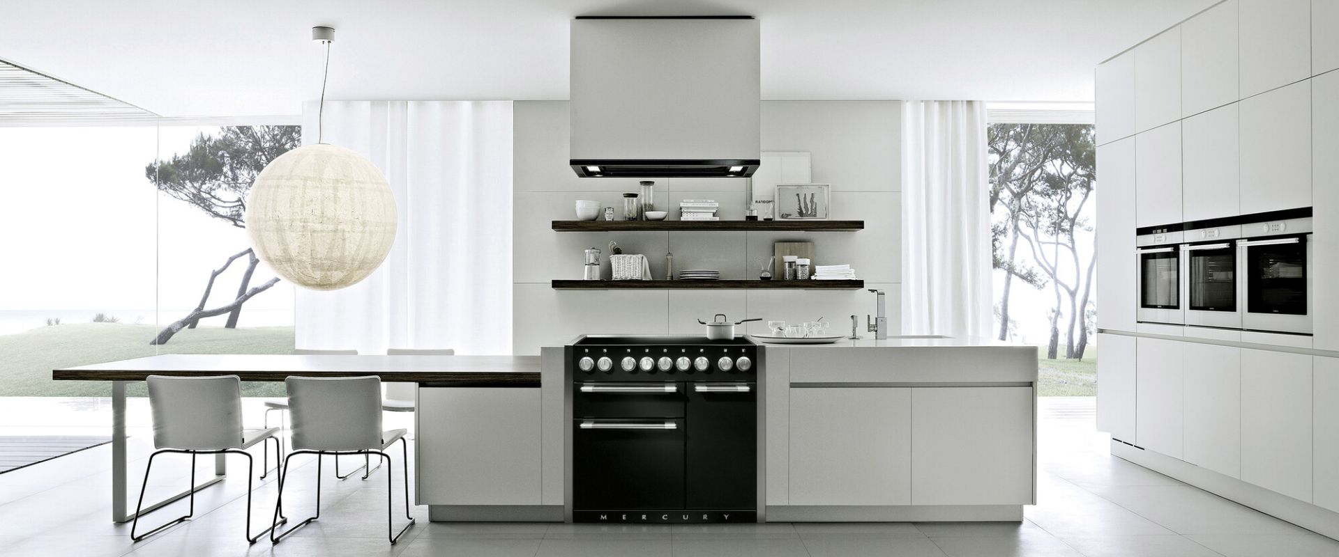 Helle, minimalistische Küche mit Kücheninsel, schwarzem Standherd, weißen Schränken, drei Einbauöfen und Panoramafenstern – ideal zur Präsentation einer Premium-Einbauküche