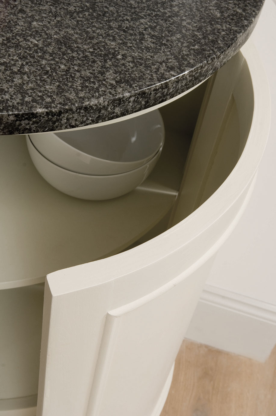 Detailansicht eines weißen Küchenschranks mit runder Granit-Arbeitsplatte und zwei weißen Schalen im Innenfach Offener weißer Küchenschrank mit runder, dunkler Granit-Arbeitsplatte und zwei gestapelten weißen Schalen im Innenraum