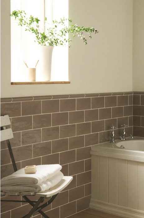 Modernes Badezimmer mit braunen Fliesen, weißen Handtüchern und Pflanze am Fenster Helles Badezimmer mit braun gefliester Wand, Badewanne, weißem Handtuchstapel auf Stuhl und Pflanze auf Fensterbrett