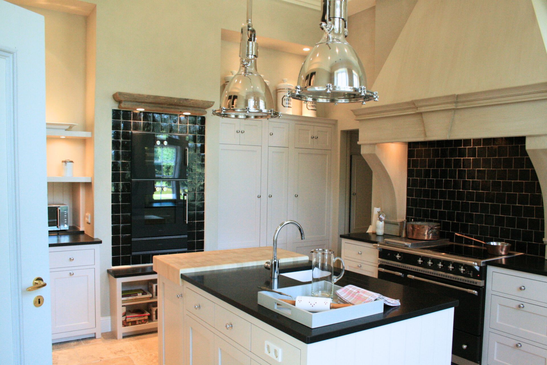 Helle Landhausküche mit Kochinsel, schwarzer Rückwand aus Metrofliesen, großem Range-Herd, weißen Einbauschränken und zwei polierten Pendelleuchten – stilvoller Kochbereich