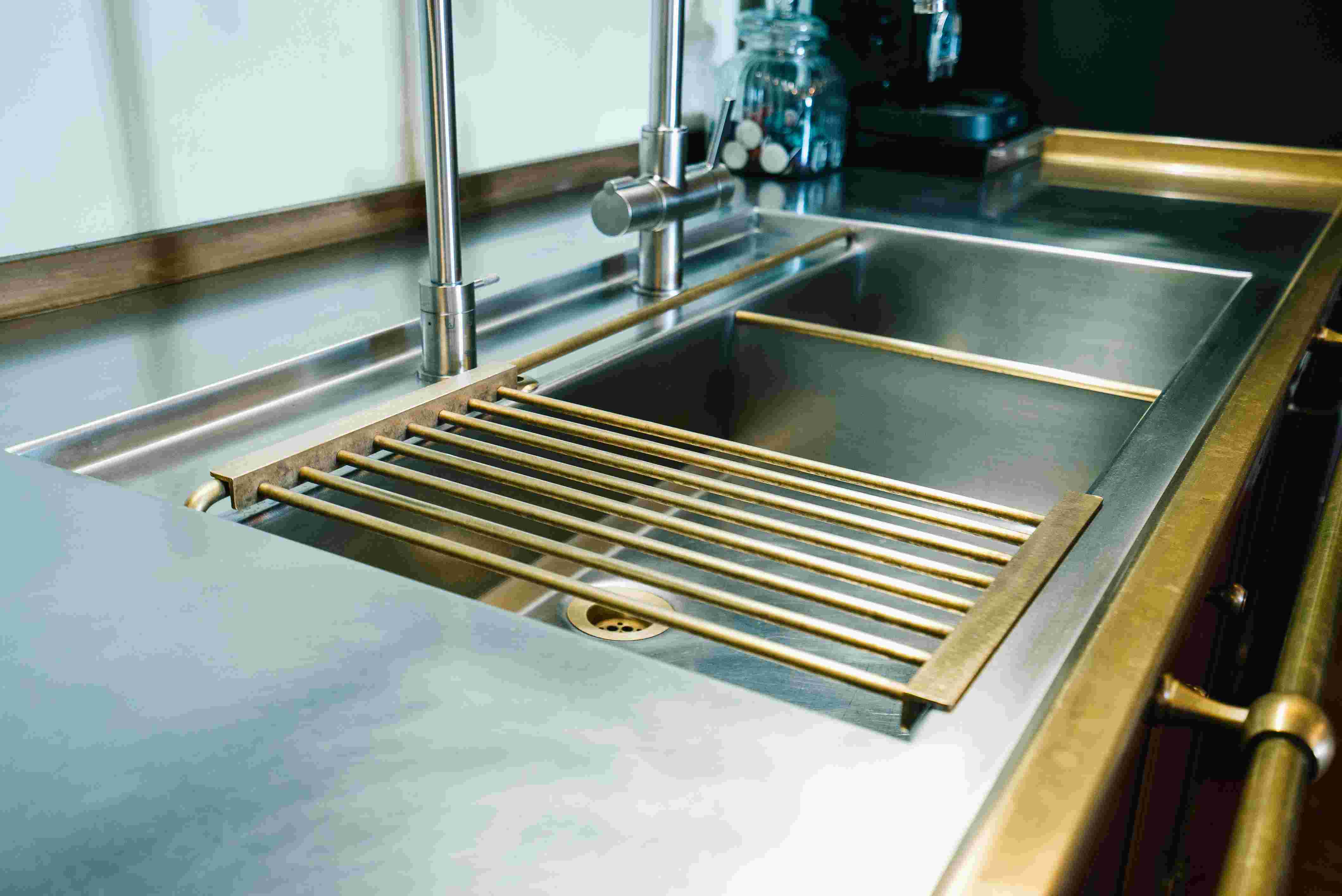 Edelstahlspüle mit zwei Wasserhähnen und goldfarbenem Abtropfgitter auf Küchentheke