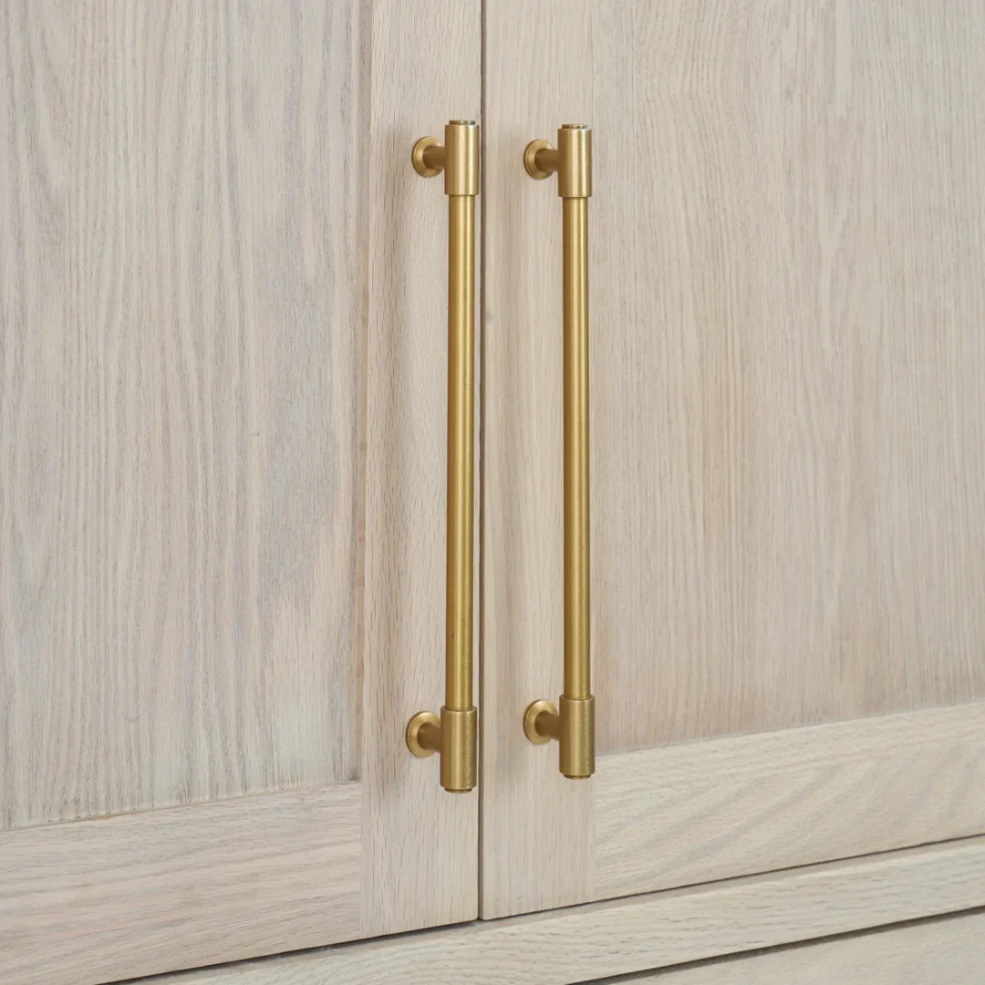 Zwei goldene Messing-Stangengriffe auf heller Holztür – eleganter Möbelgriff für Schrank, Küche oder Kommode