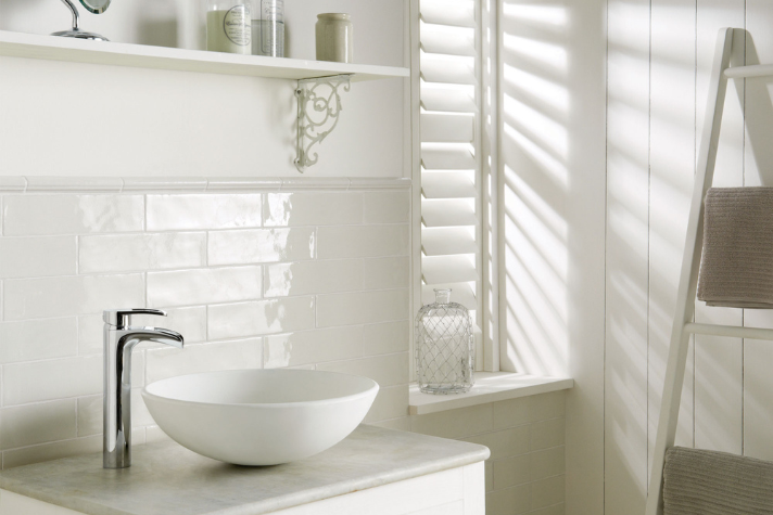 Modernes Badezimmer mit weißem Waschbecken und stilvollem Wasserhahn Helles Badezimmer mit rundem weißen Aufsatzwaschbecken, Chromarmatur, gefliestem Hintergrund und dekorativen Accessoires auf Regal