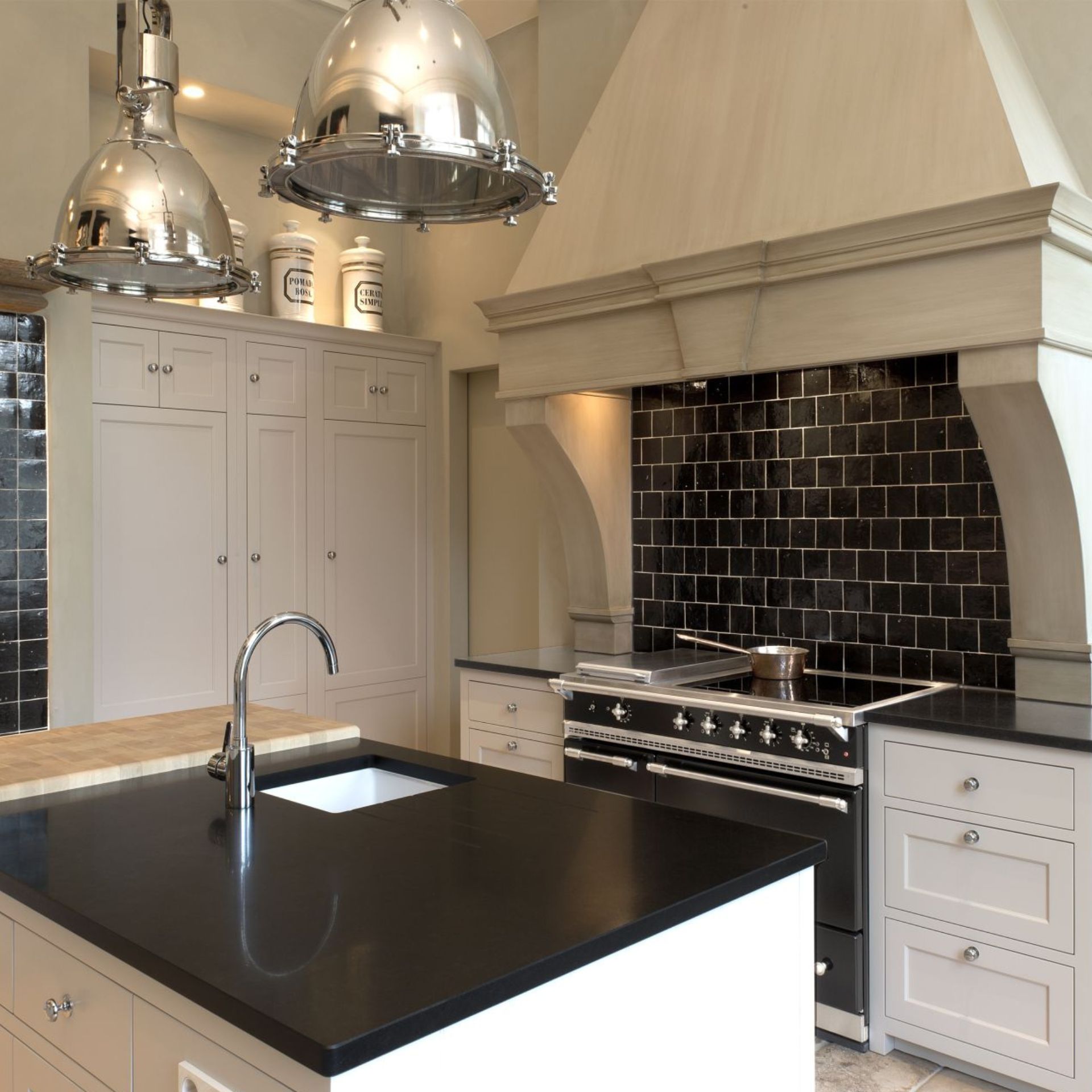 Elegante Kücheninsel mit schwarzer Quarz-Arbeitsplatte, integrierter Spüle und Chromarmatur; passend zu Range Cooker und schwarzer Fliesenrückwand in moderner Landhausküche